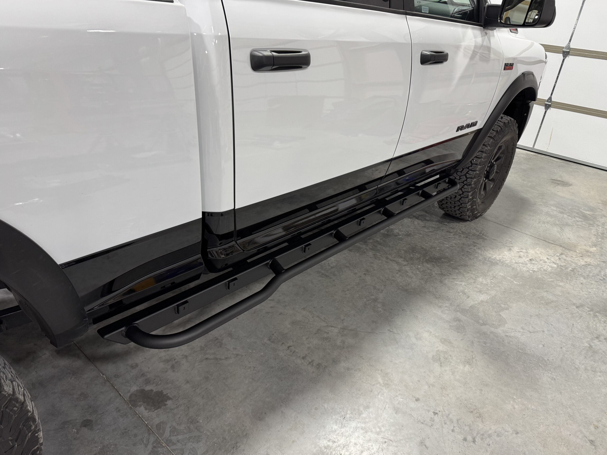 Slider fitted along the rocker of a white Ram in a garage, seen from the front wheel back