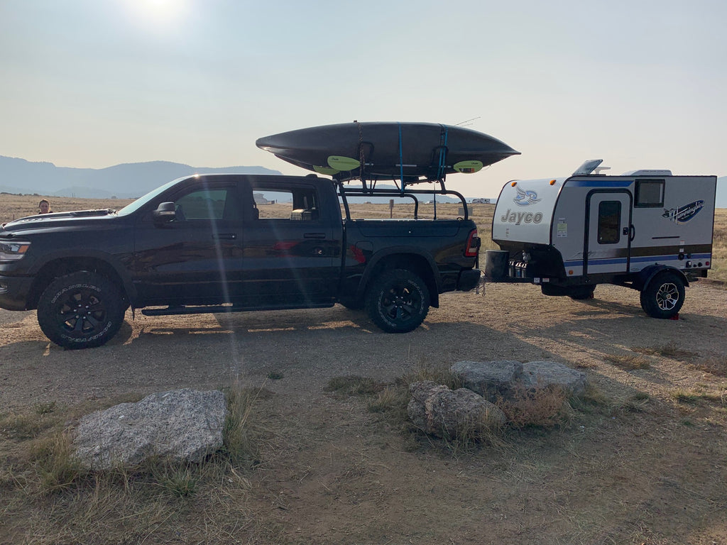 Side view of the black Ram 1500 carrying a boat on the rack, trailer hitched behind
