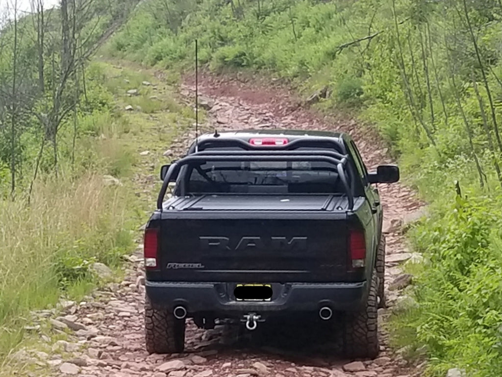 Black Ram climbing a rocky wooded trail, seen from behind with the rack over the bed