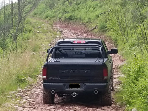 Black Ram climbing a rocky wooded trail, seen from behind with the rack over the bed