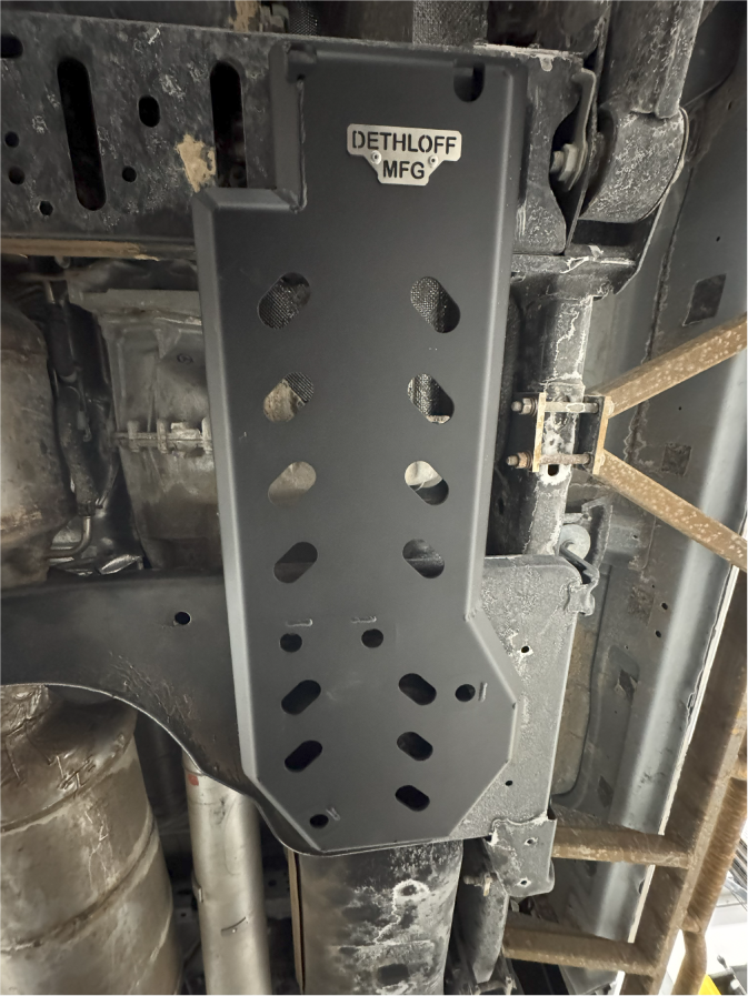 The guard bolted up under the truck alongside the exhaust, badge at the top