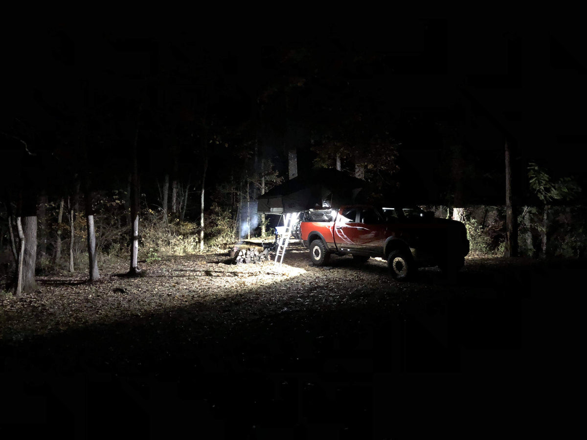 A campsite at night lit by the truck's rack lights, awning and chairs in the beam