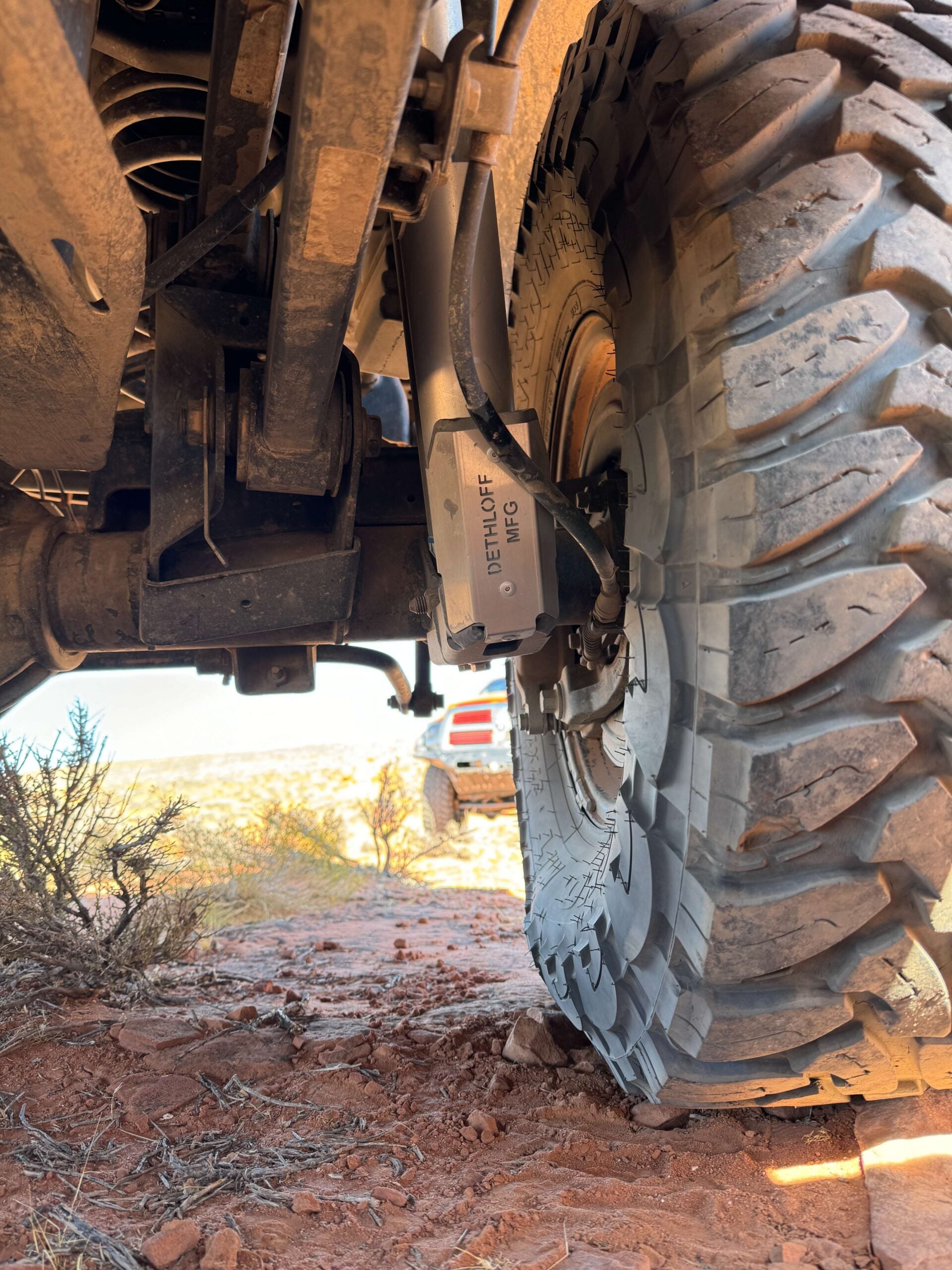 Guard fitted on the rear shock, seen from under the truck out onto red desert ground