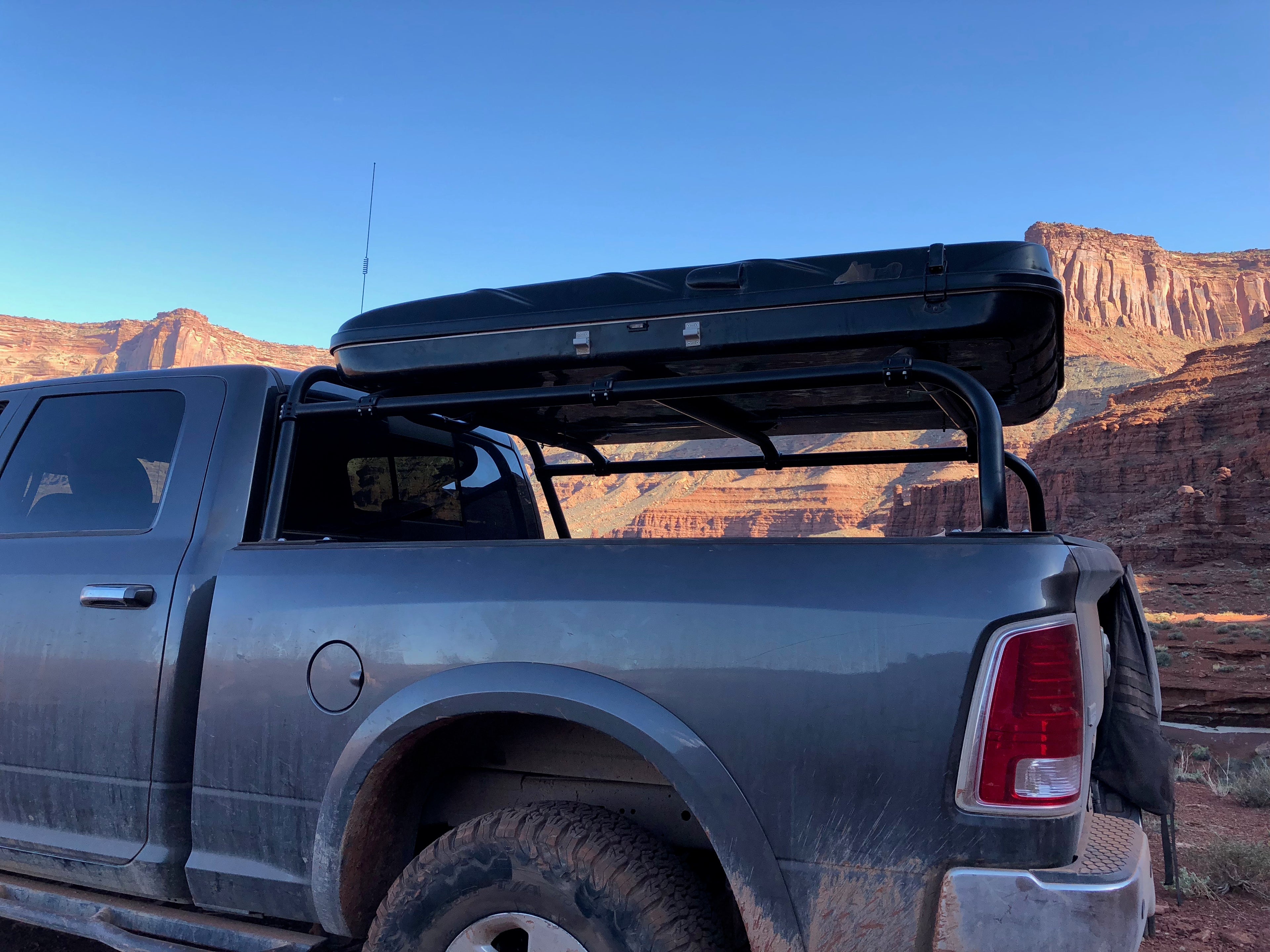 Rear quarter of the grey Ram, roof box on the rack against red cliffs