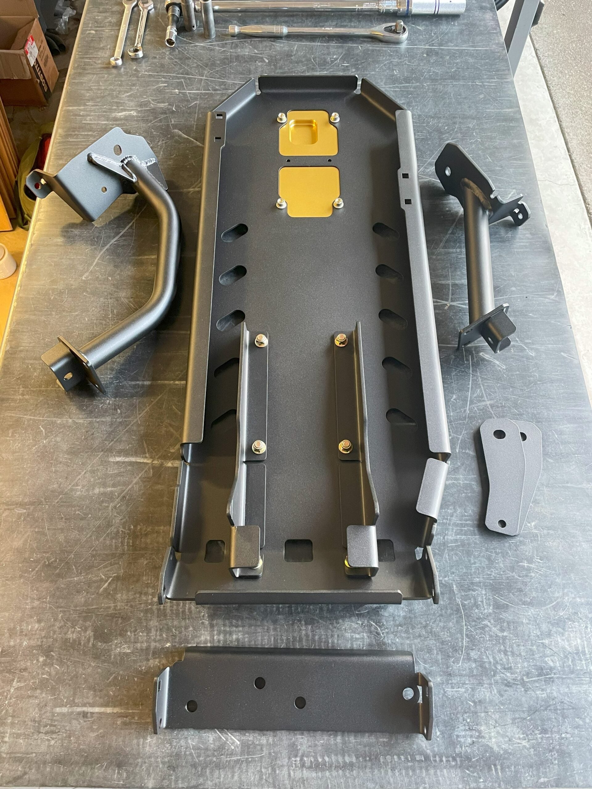 The complete armor kit laid out on a workbench from above: main plate, bar guards and brackets