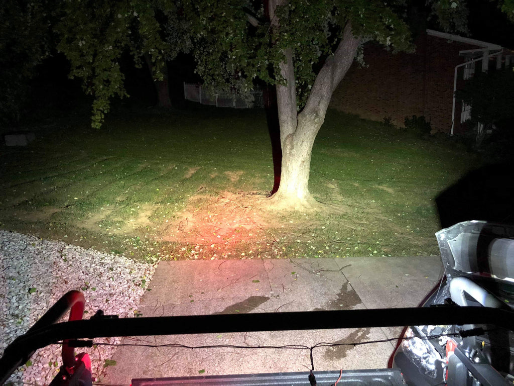 The beam from the rack lights spread across a lawn and a tree at night
