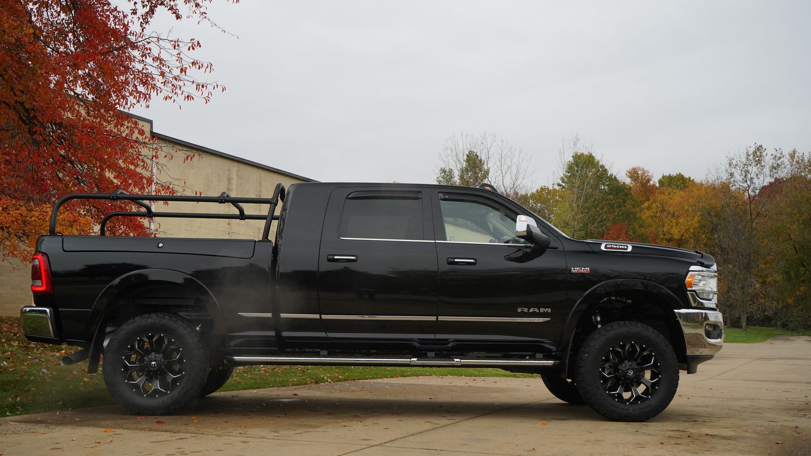 Full side profile of the black Ram, rack running the length of the bed and autumn trees behind