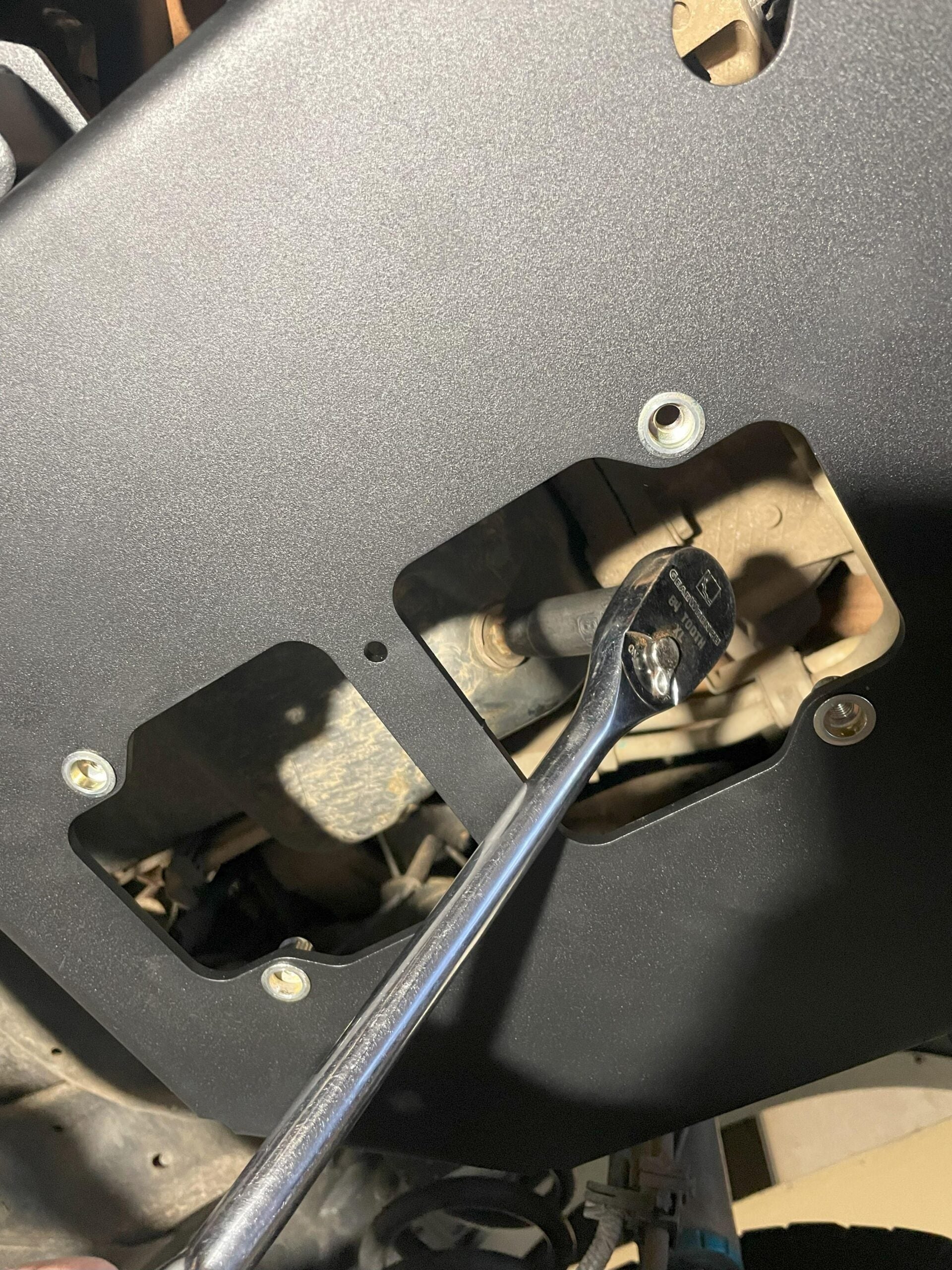 A ratchet reaching through the opened service port to reach a component behind the plate