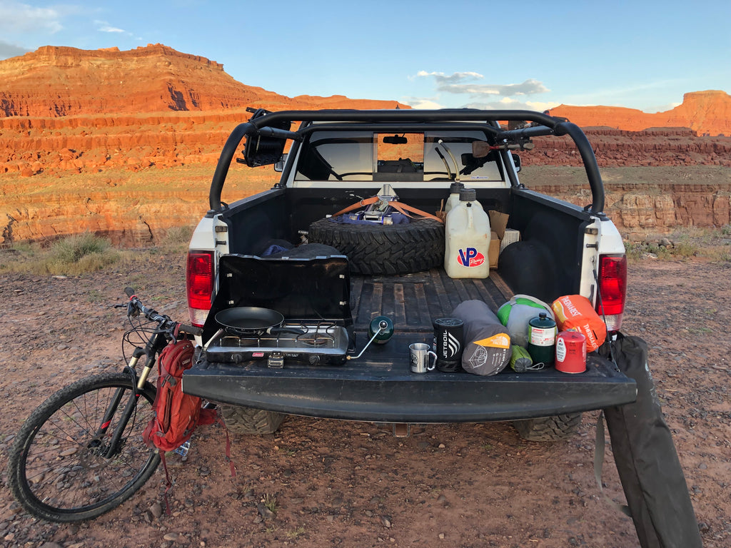 Tailgate down at a desert camp, bed full of gear with helmets and a bike at the tailgate