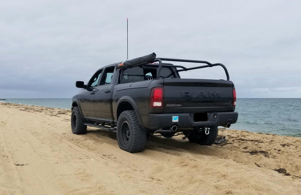 Black Ram parked on a beach at the water's edge, rack fitted over the bed