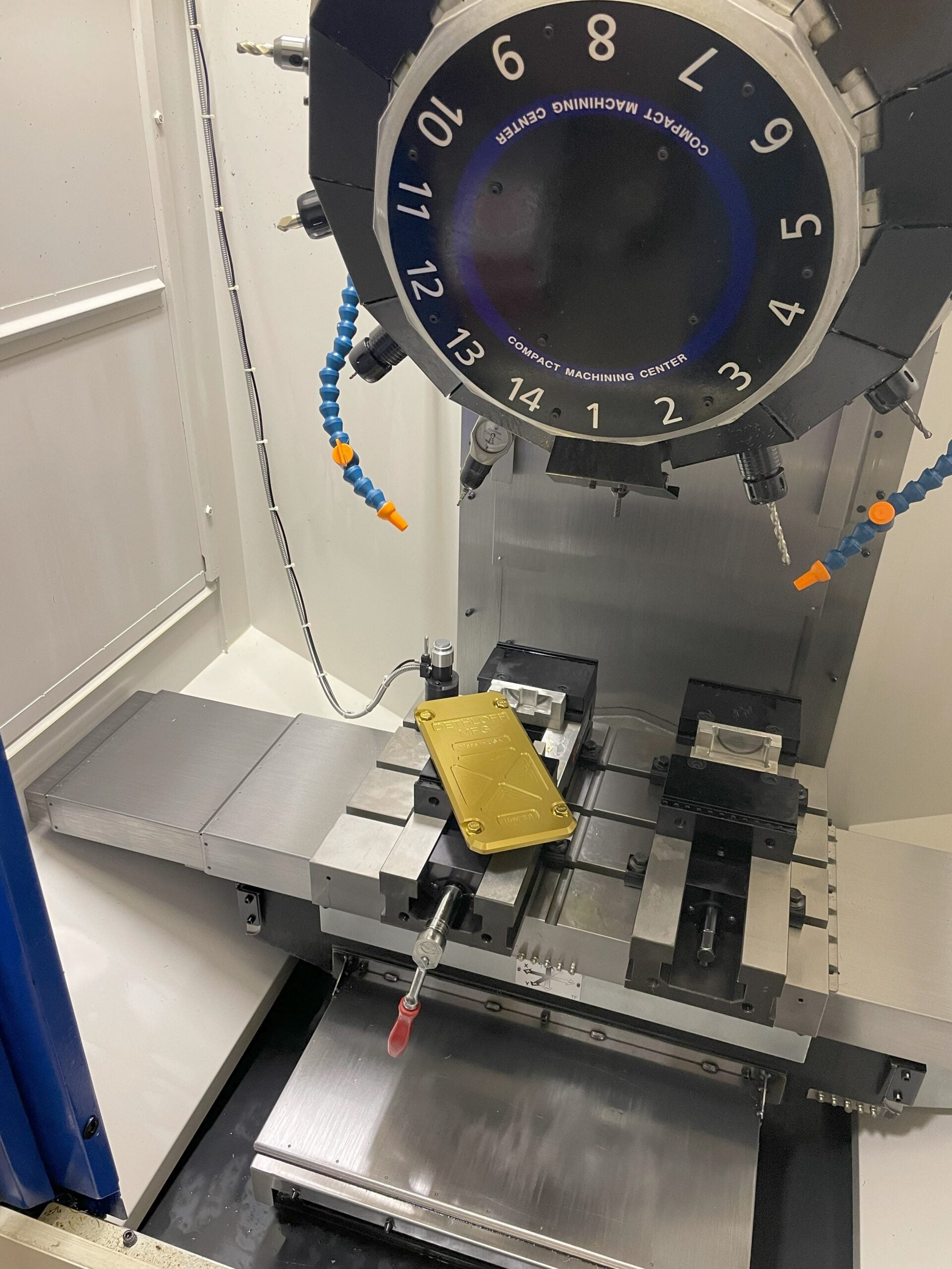 A gold panel held in the vise of a CNC machining center