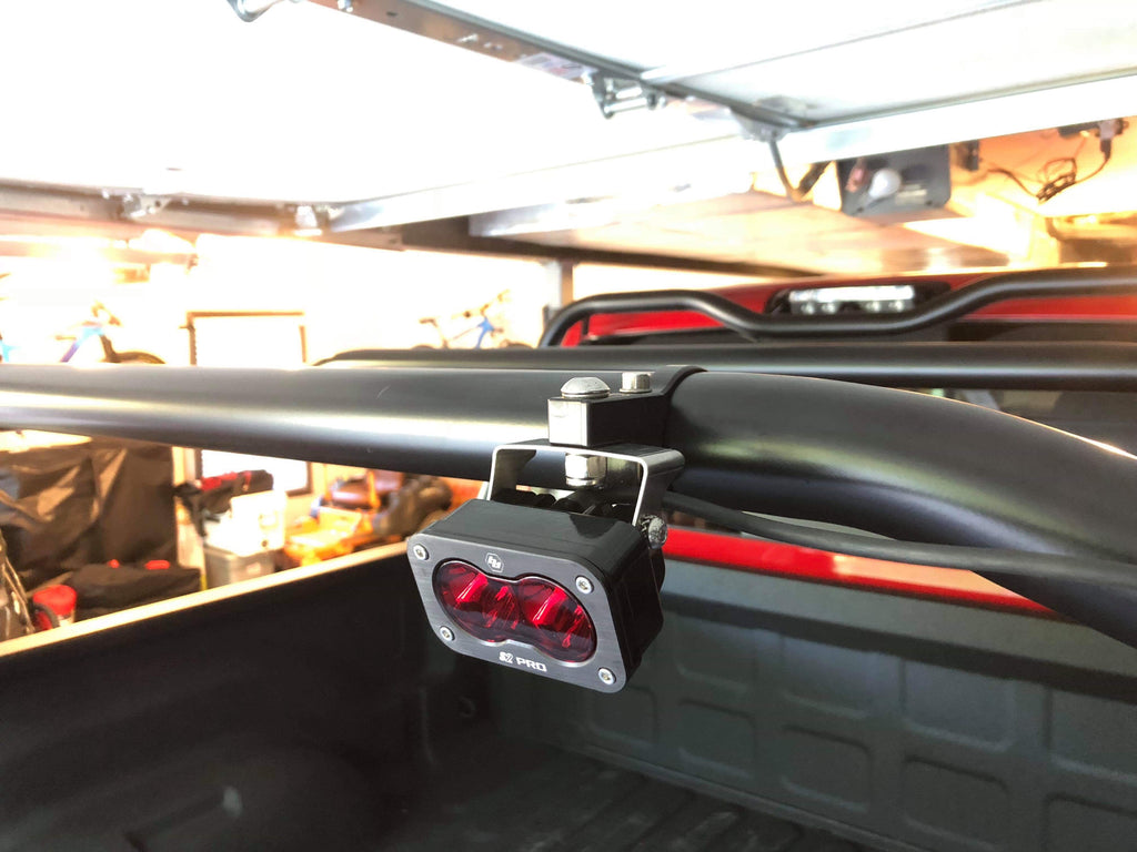 A light pod clamped to the rack's side bar in a garage, lens facing out over the bed