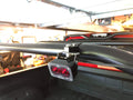 A light pod clamped to the rack's side bar in a garage, lens facing out over the bed