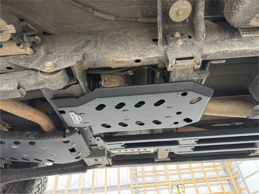 The guard in place under a truck on a lift, exhaust and driveshaft running alongside