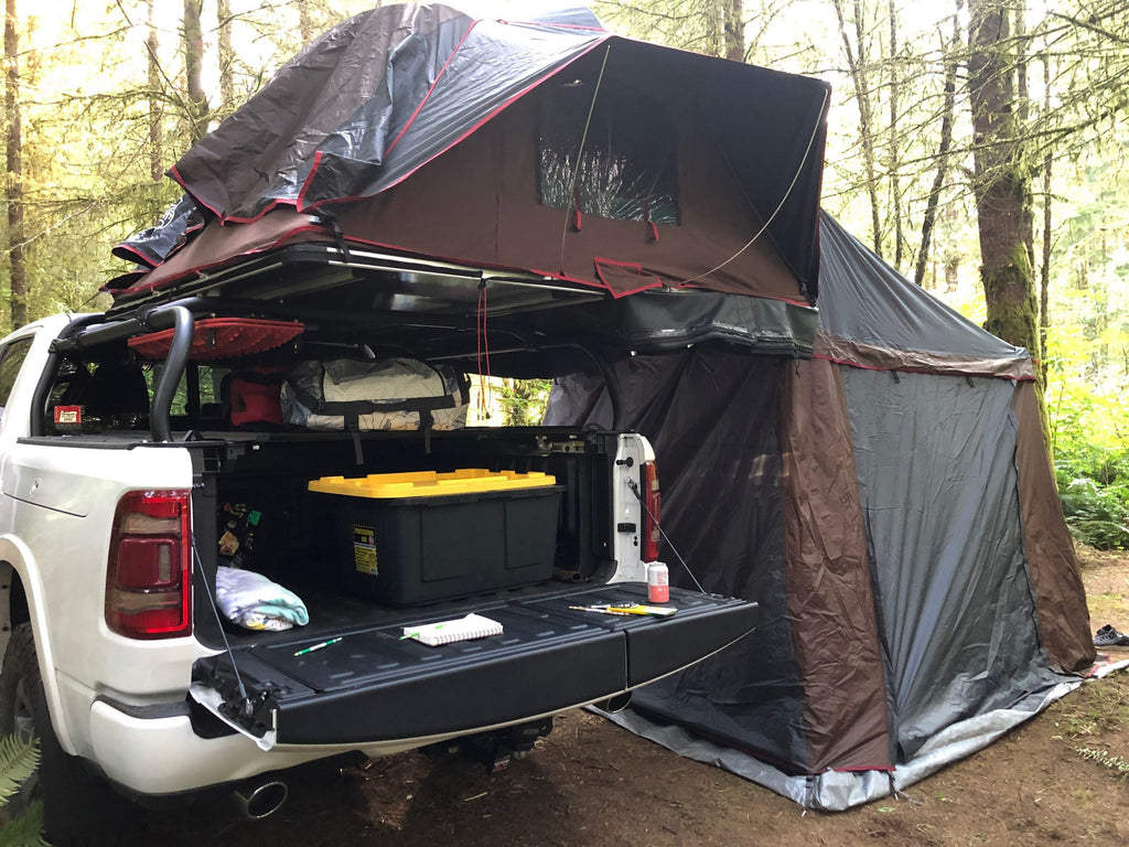 White Ram 1500 in the woods, roof tent open on the rack with its annex hanging past the open tailgate