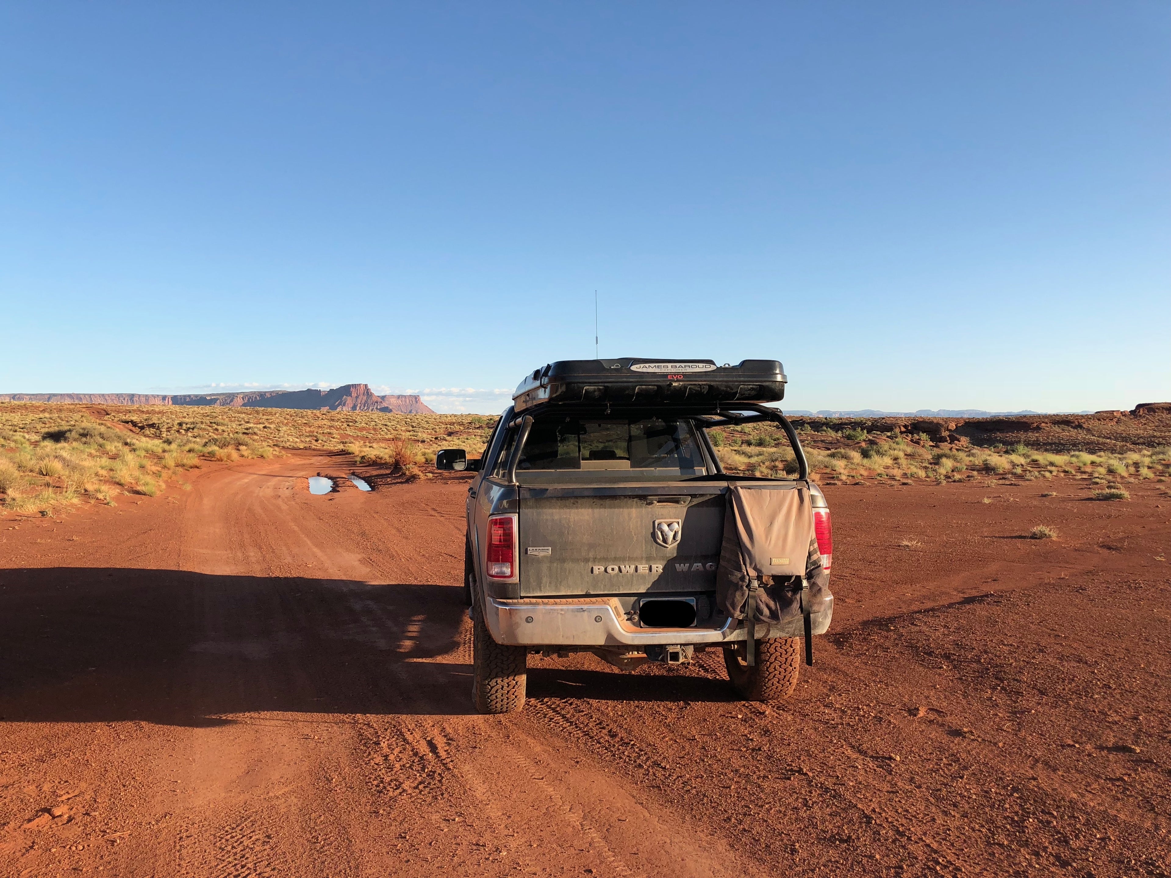 White Power Wagon driving away down a red dirt road, roof box on the rack