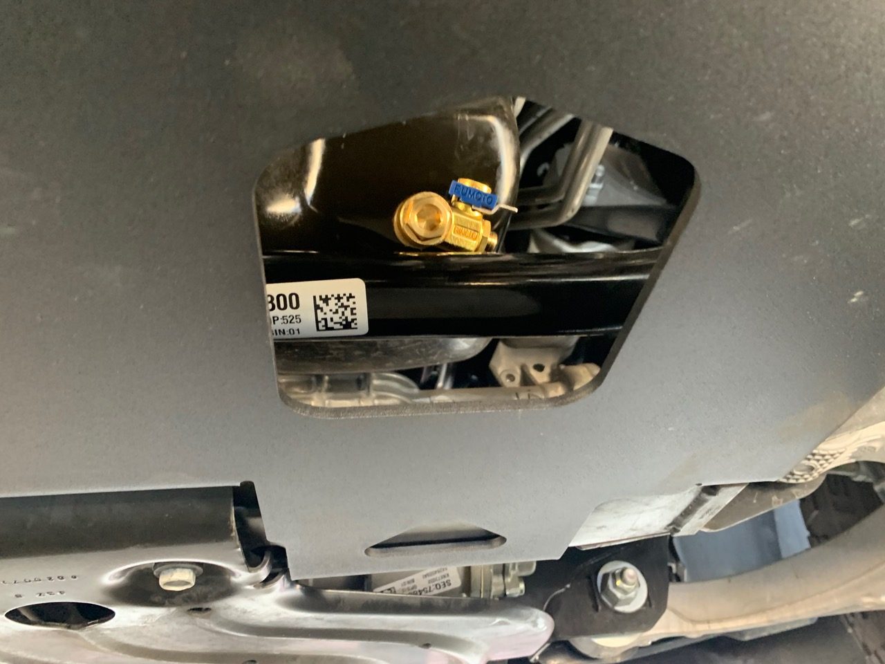 A service opening in the plate with a yellow fitting and a barcode label visible behind it