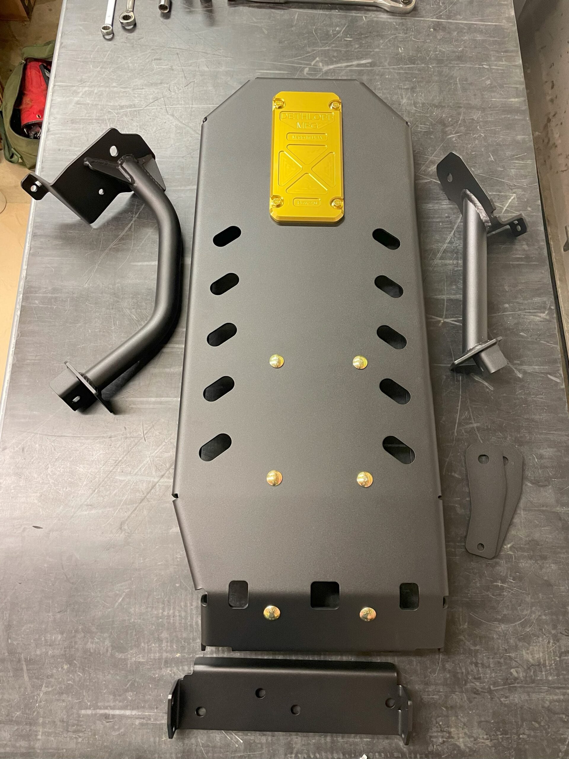 Skid plate on a steel workbench with its mounting brackets and tubular bar guards laid out beside it