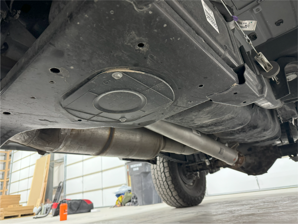 Under the truck looking back along the exhaust, the tank and its access cover overhead