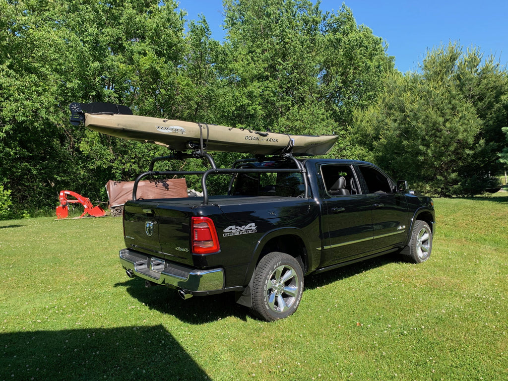Rear quarter of the dark blue Ram 1500 on a lawn, sea kayak carried overhead