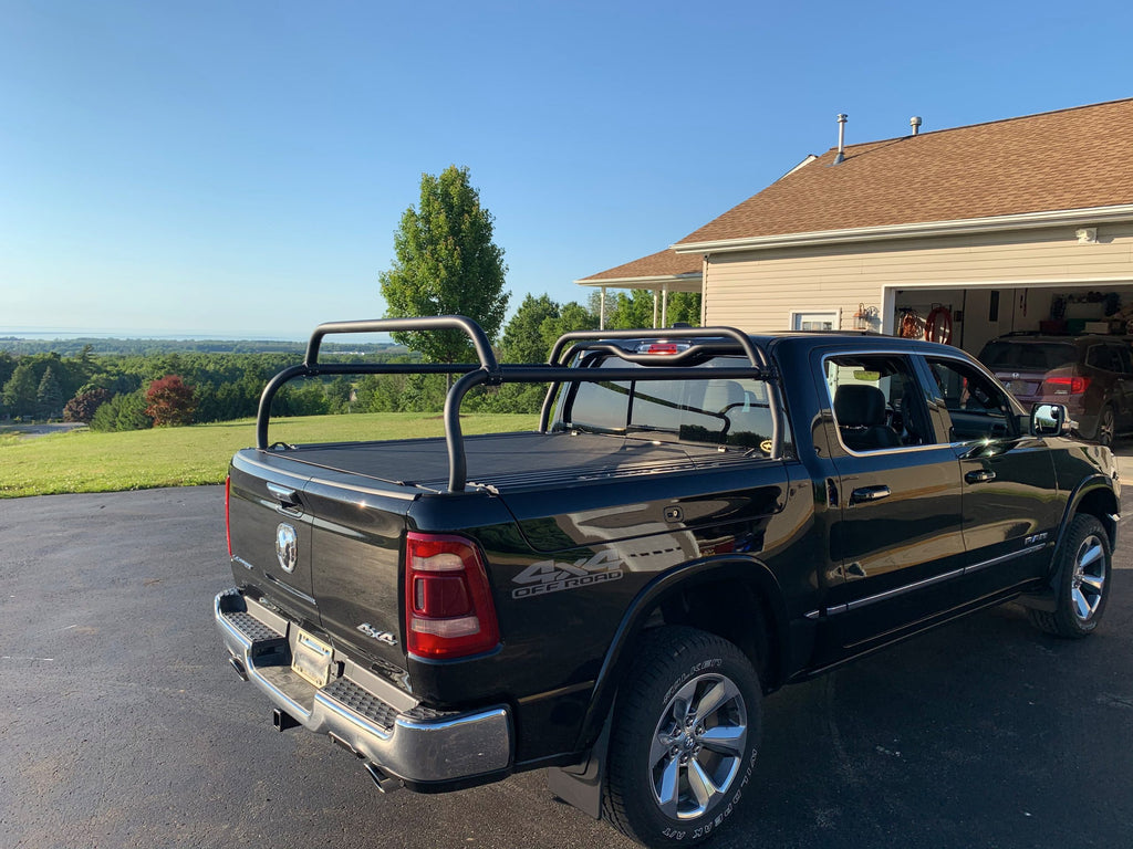 Rear quarter of a black Ram on a driveway, crossbars above a closed tonneau