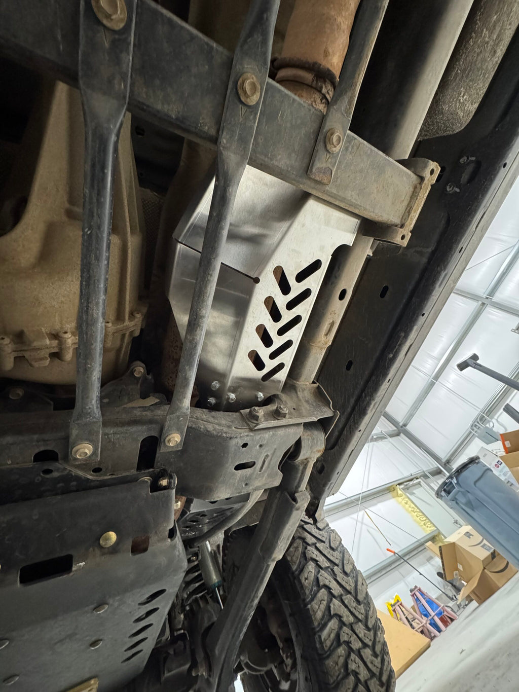 The bare aluminium guard bolted over the catalytic converter, chevron slots across its face