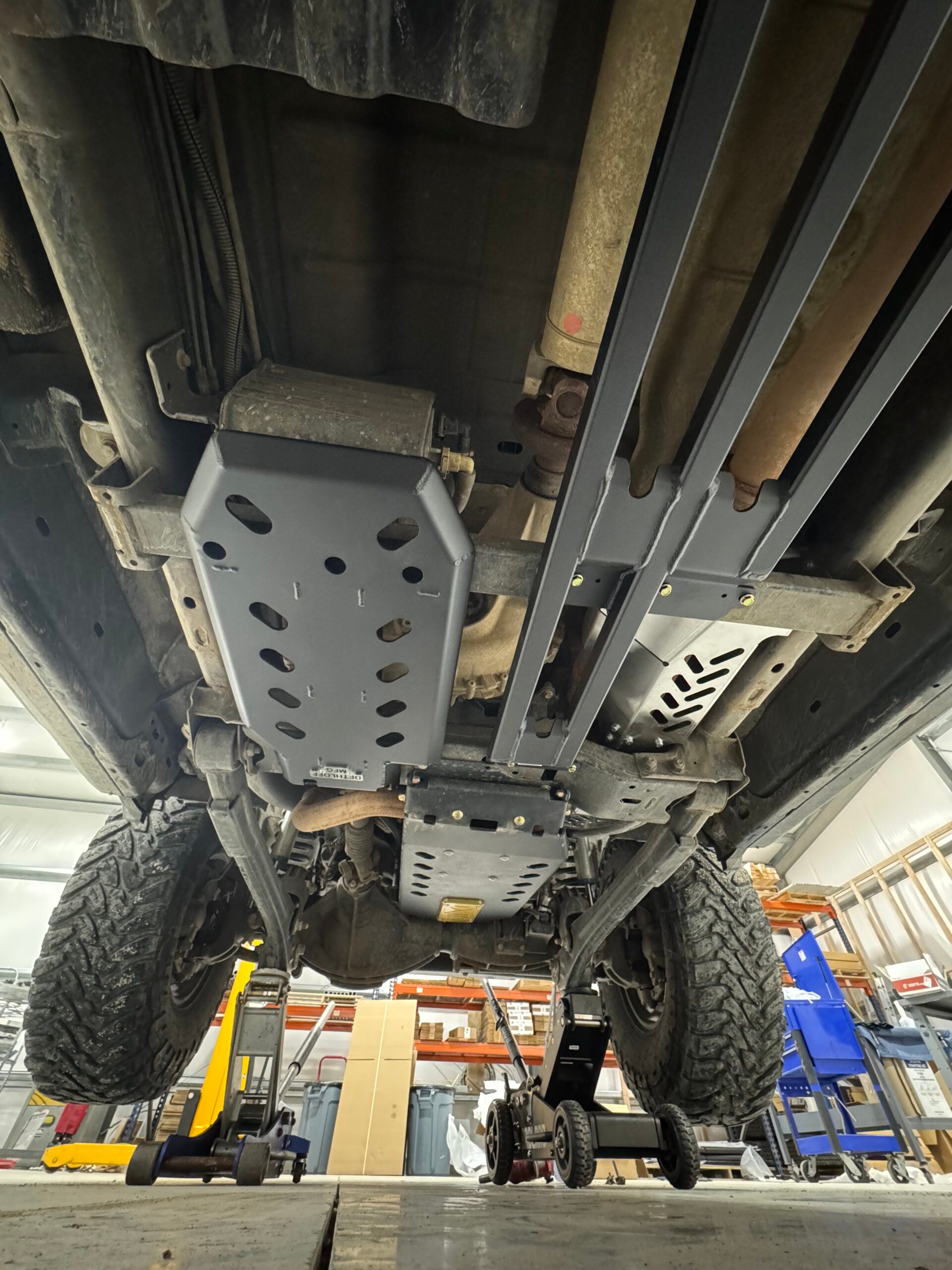 Looking straight up at the underbody on a lift, the bare aluminium guard sitting behind the grey Dethloff skid plates