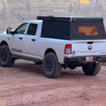 White Ram HD with a bed topper parked on a dirt track, rear bumper fitted, seen from the side and rear