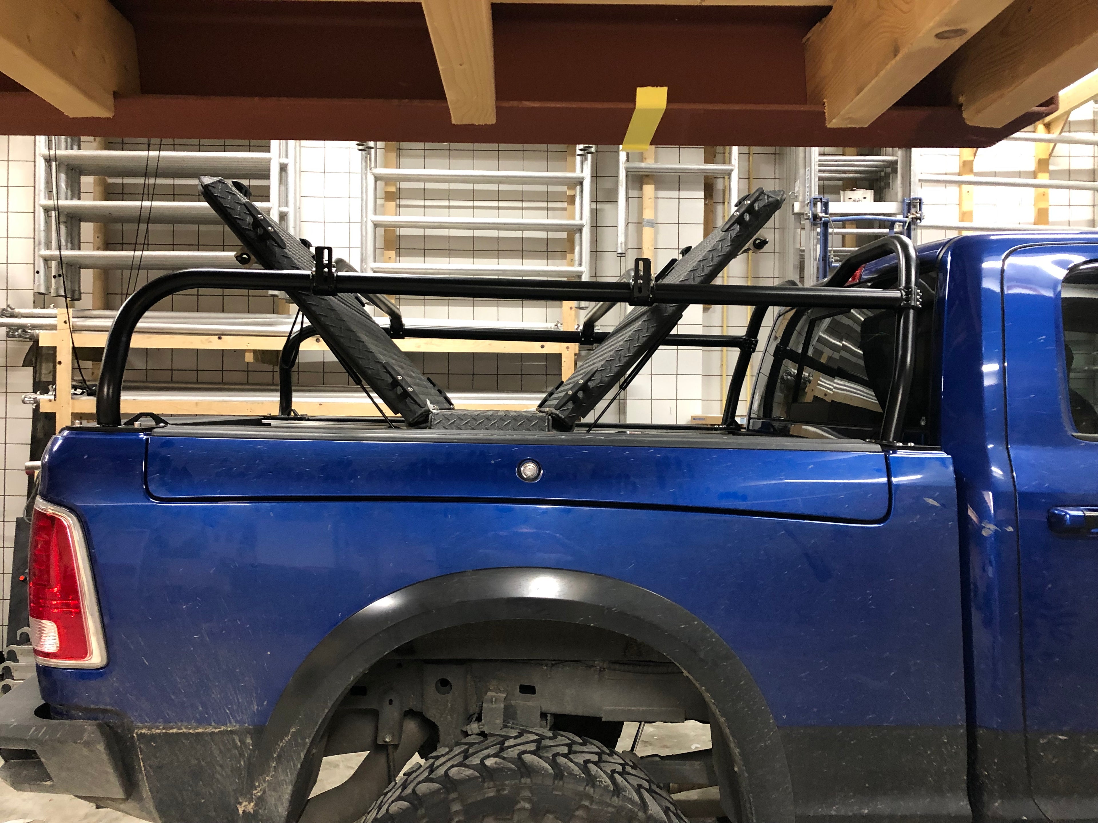 Side view of the blue Ram in the garage, tonneau panels raised within the rack