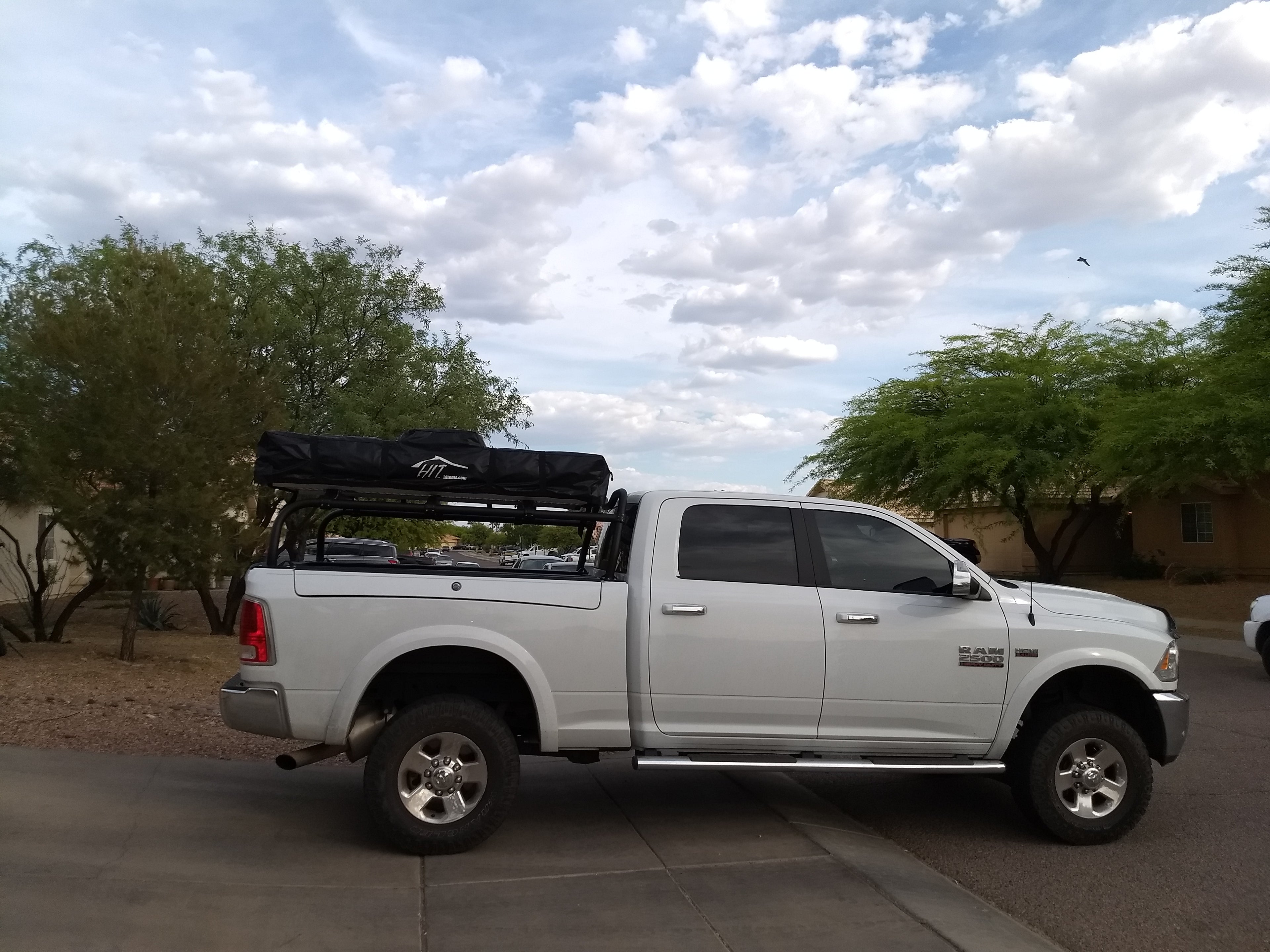 White Ram on a driveway, closed roof tent on the rack, desert trees behind