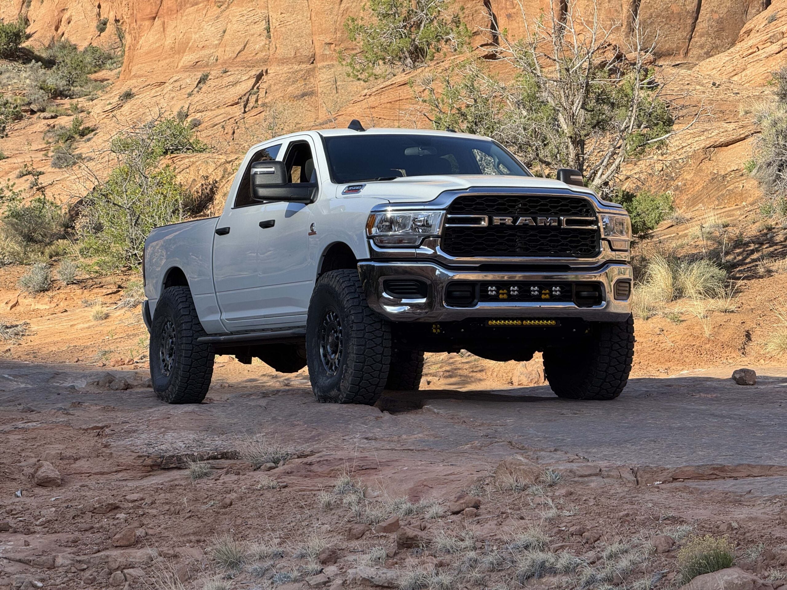 White Ram parked on slickrock below a sandstone wall, sliders along the rockers