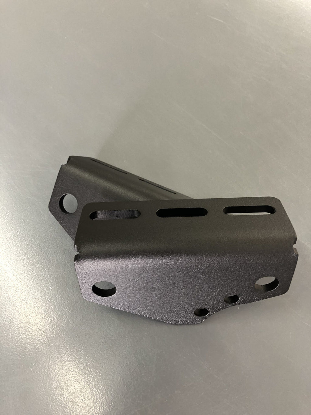 A single bracket on the bench, its slotted faces and bolt holes in view
