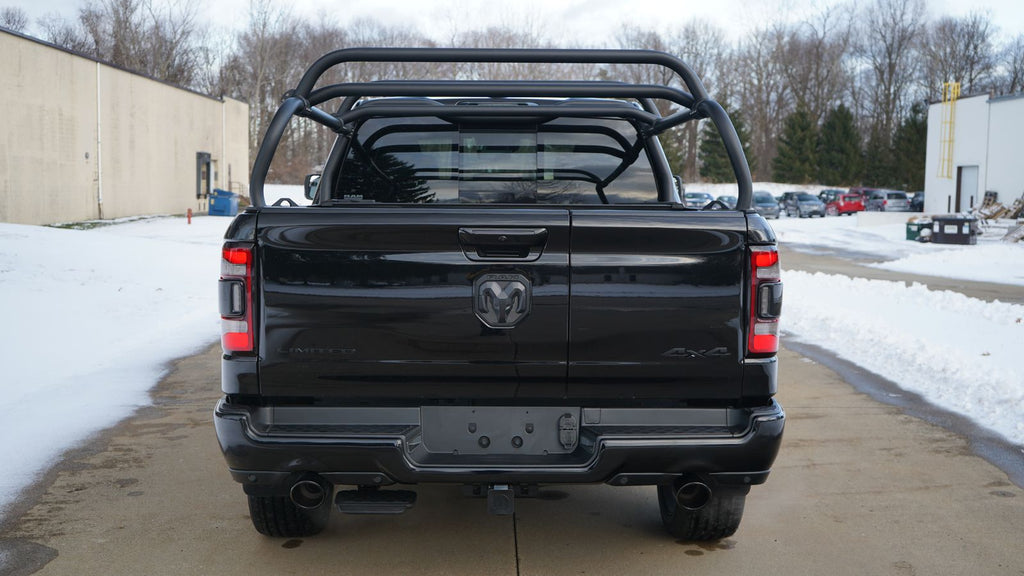 Straight rear view of the black Ram 1500 on a snowy lot, crossbars above a closed tonneau