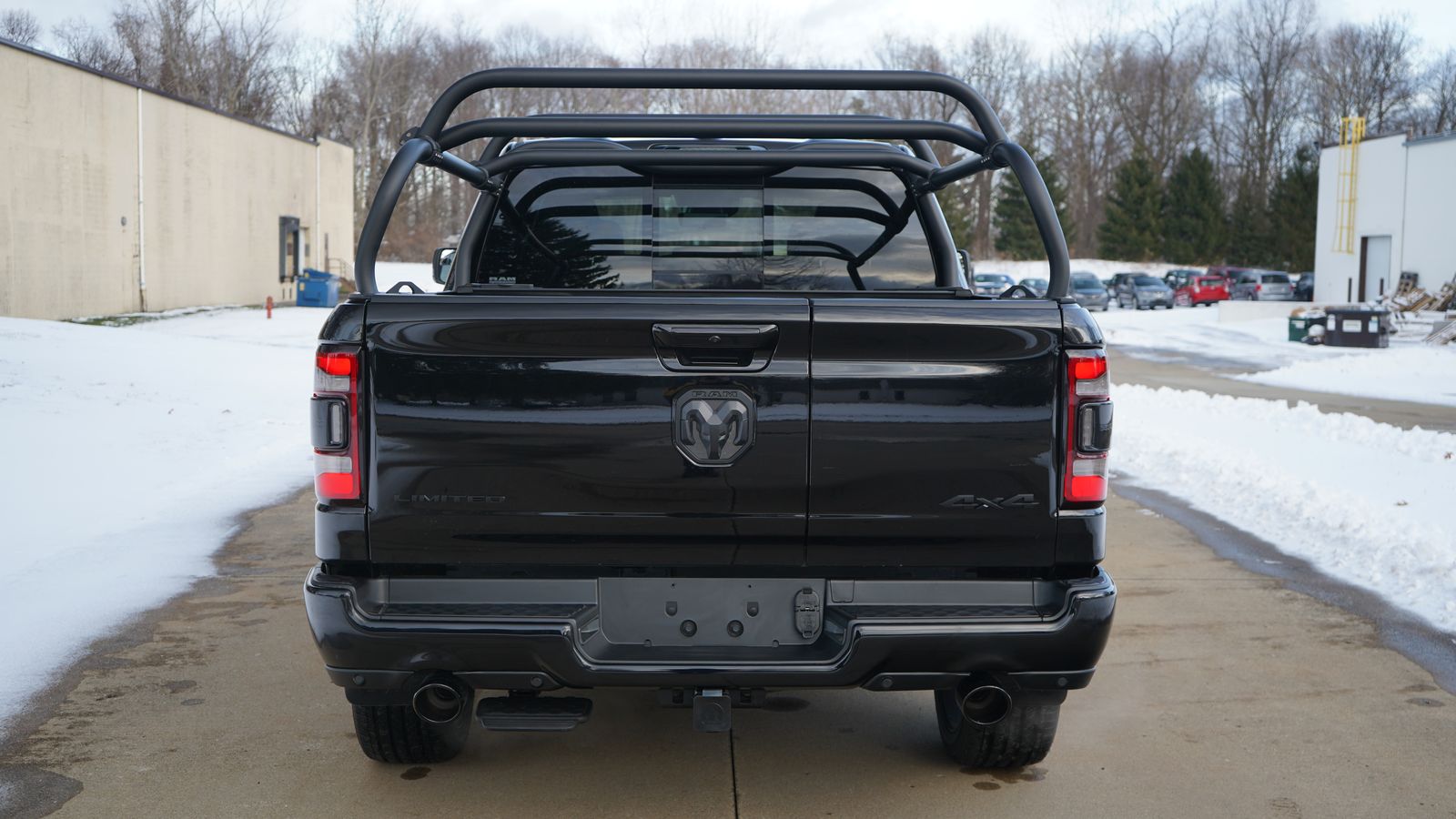 Straight rear view of the black Ram 1500 on a snowy lot, crossbars above a closed tonneau
