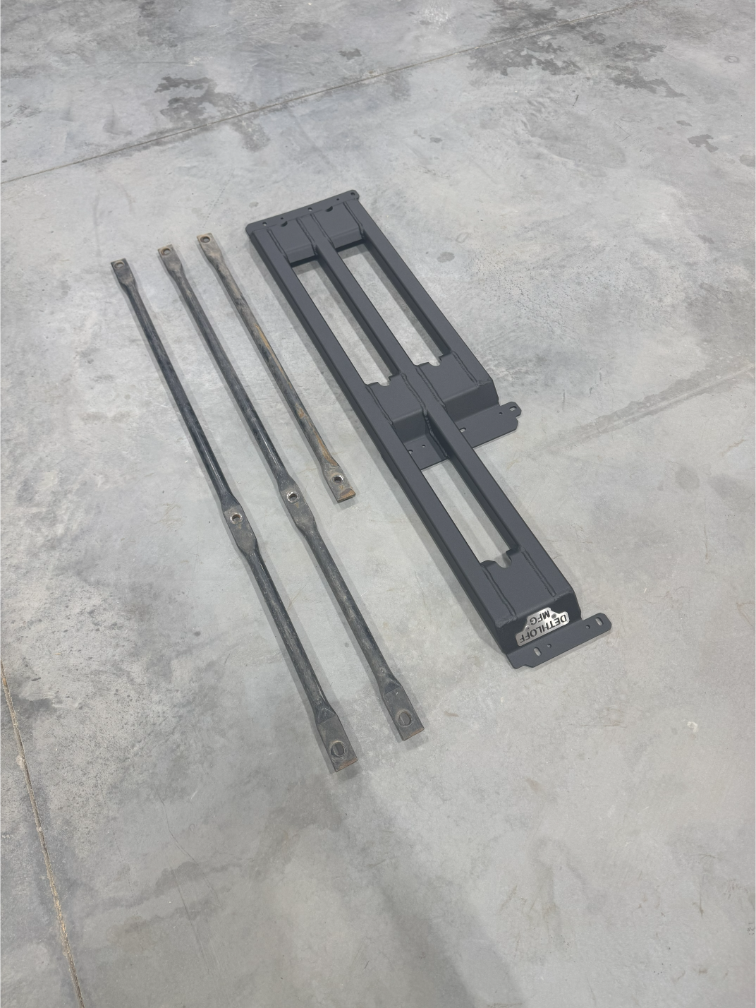 The three-bar frame and its support bars laid out on a concrete floor