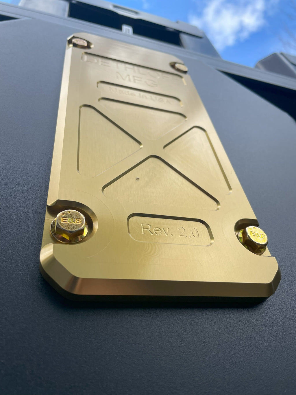 Gold anodized service panel bolted into the black skid plate, marked Rev 2.0