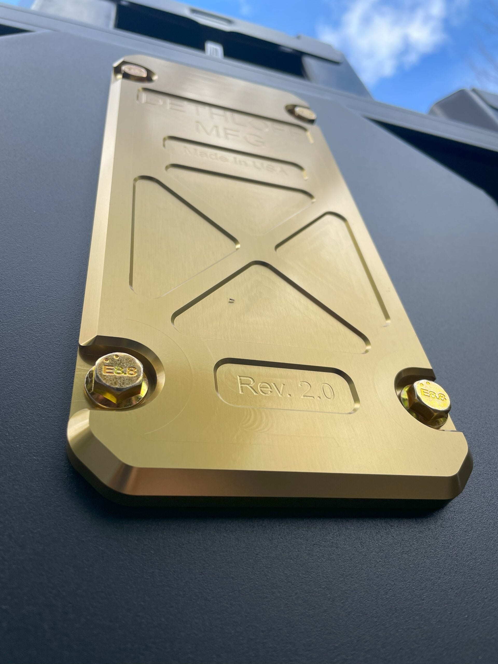 Gold anodized service panel bolted into the black skid plate, marked Rev 2.0