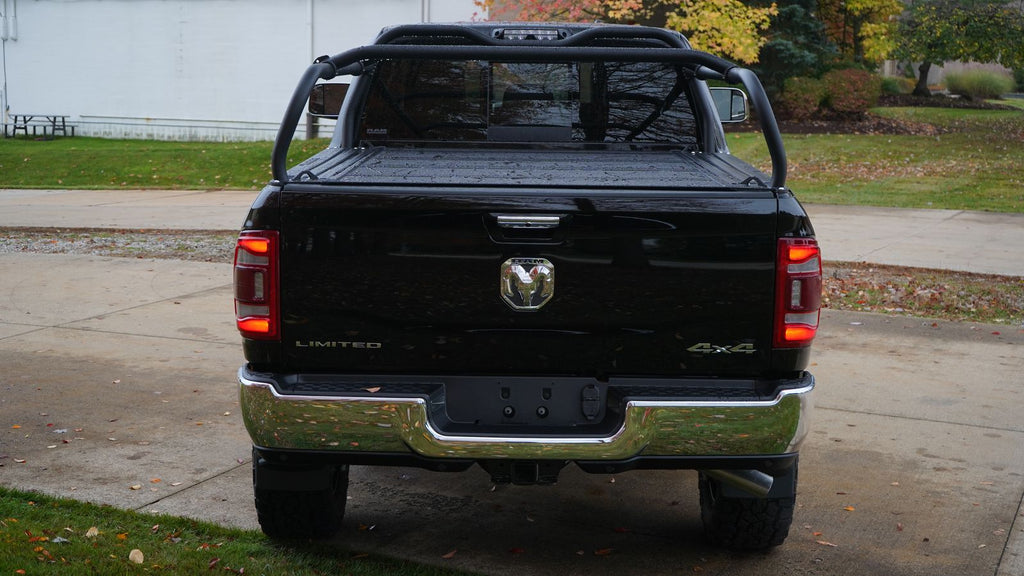 Straight rear view of the black Ram on a driveway, rack legs rising above a closed tonneau